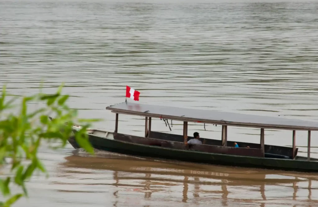 A boat with a Peruvian flag sails across the Tambopata River